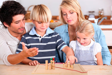 Familie stellt gemeinsam mit dem Systembrett eine Aufstellung. Der Junge bewegt eine Figur.